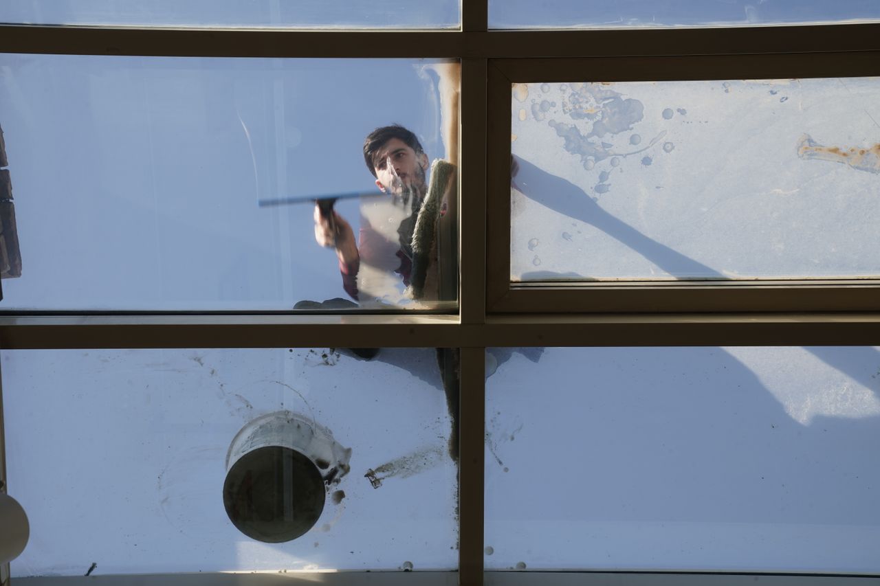 Un laveur de vitres masculin nettoie la toiture vitrée extérieure depuis le dessus avec un outil en plein jour.